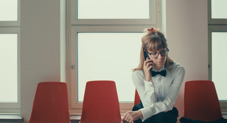 Olga Kosanović sitzt auf einem Stuhl und telefoniert. Filmstill auf NOCH LANGE KEINE LIPIZZANER.