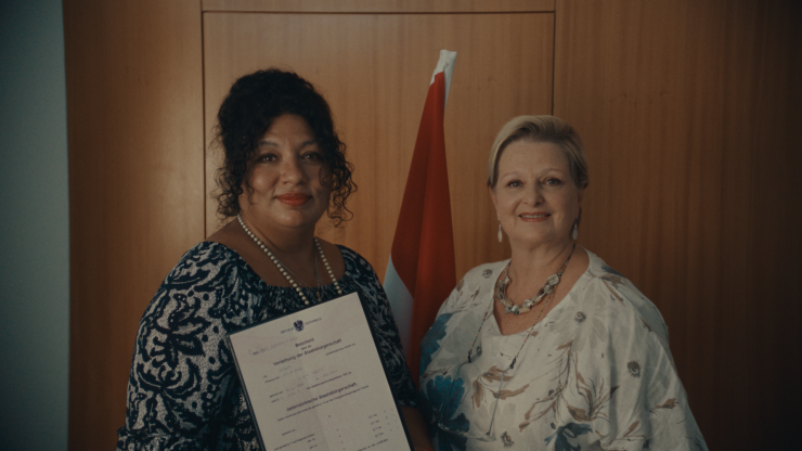 Zwei Frauen blicken in die Kamera. Die Staatsbürgerschaftsurkunde wurde an eine der Frauen übergeben.