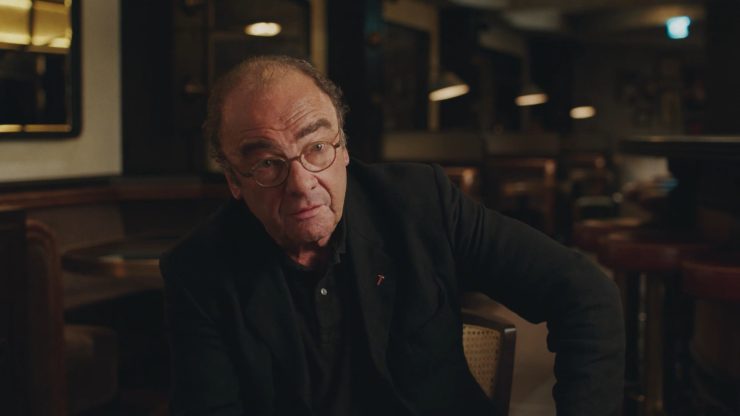 Ein Mann sitzt in einem leeren Wirtshaus mit schwarzem Hemd.