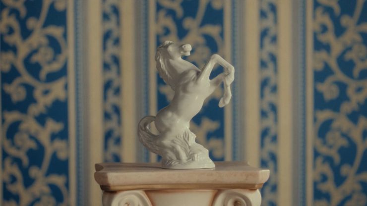 Eine weiße Lipizzaner Statue steht vor einer blau gestreiften Tapete.