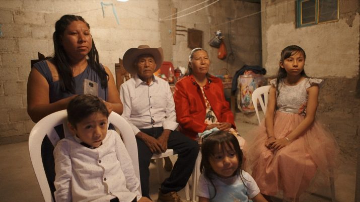 Eine Familie sitzt auf Plastikstühlen in einem kahlen Raum.