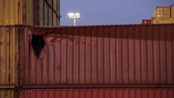 Ein roter Schiffscontainer mit einem Loch an der linken Ecke