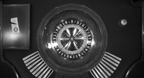 Roulettekessel mit Zahlen von 1 bis 36 und 0, umgeben von Spielchips auf einem Holztisch