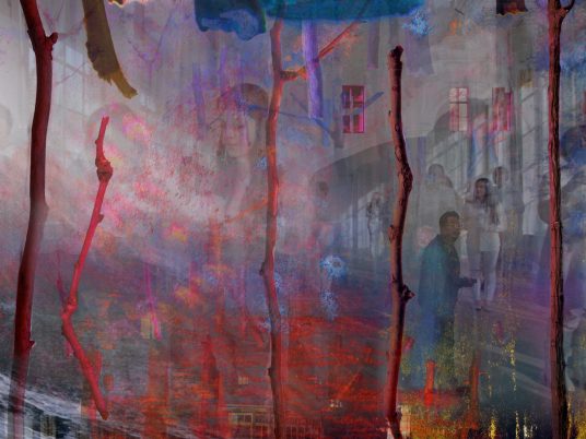 Mehrere dünne, vertikale Äste vor einem mehrschichtigen, farbintensiven Hintergrund mit Gebäuden und Menschen in einem Innenhof.