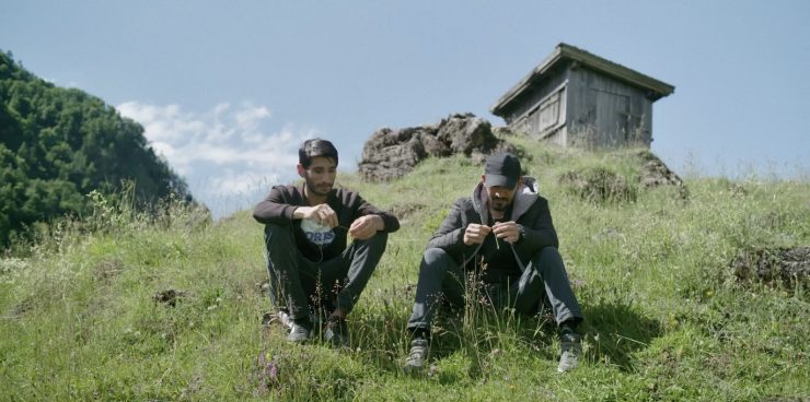 Zwie junge Männer sitzen in der Wiese auf einem Berg.