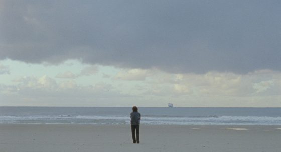 Eine Person steht am Strand mit Blick auf das Meer.