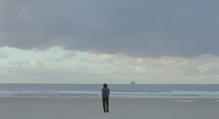 Eine Person steht am Strand mit Blick auf das Meer.