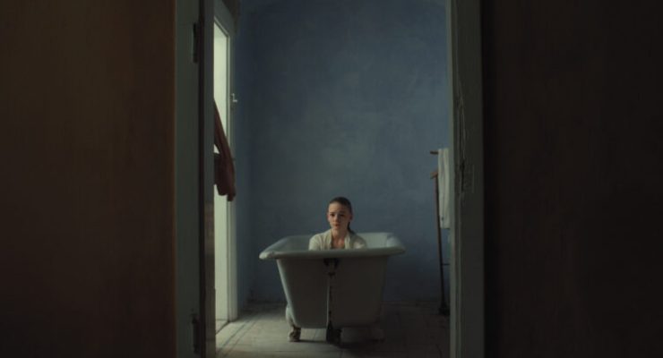 Person sitzt in einer freistehenden Badewanne in einem schmalen, dunklen Raum mit blauer Wand.