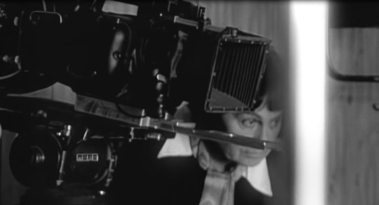 Nahaufnahme einer Person hinter einer alten Filmkamera mit Balgen und Sucher.