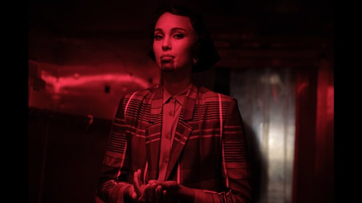 Eine Frau rot beleuchtet in einem karrierten Sakko.