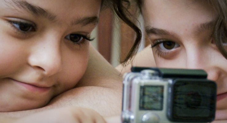 Zwei Mädchen, sitzen nah beieinander, eine hält eine Kamera.