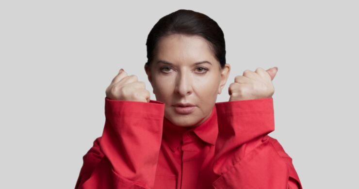 Marina Abramović in einem rotem Oberteil zeigt beide Fäuste nach oben