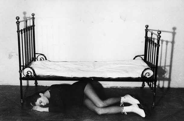Frau liegt seitlich auf dem Boden unter einem schmiedeeisernen Bett mit weißen Schnürstiefeln