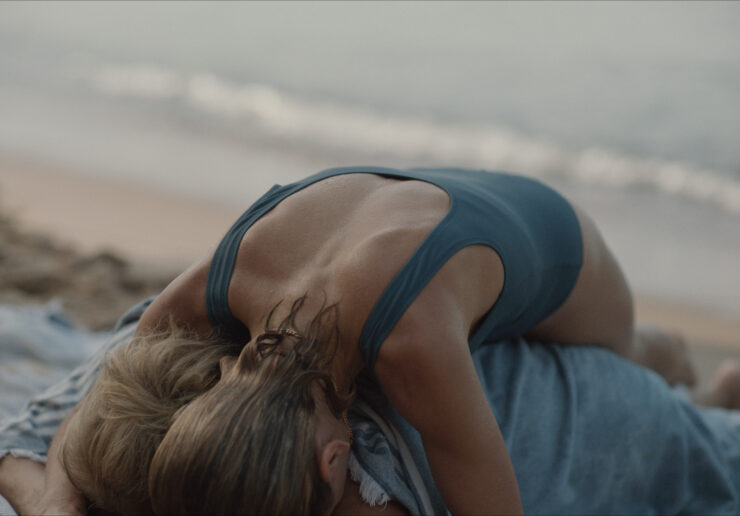 Frau in blauem Badeanzug liegt am Strand auf einer anderen Person