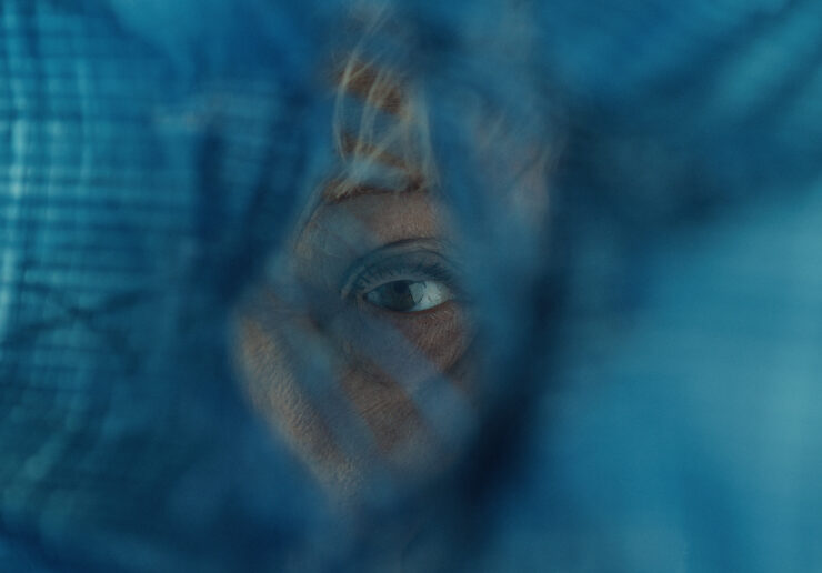 Nahaufnahme eines Auges hinter einem unscharfen, blauen Netz oder Gewebe